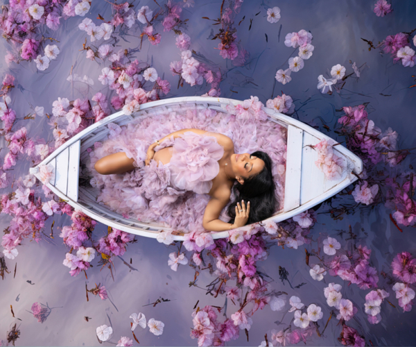 Maternity in Bloom — Floating in Petals Pregnant woman lying in a white boat filled with pink petals