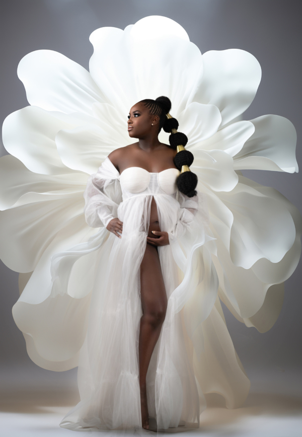 Modern Maternity Goddess with Floral Backdrop Pregnant Black woman in a white maternity gown posing in front