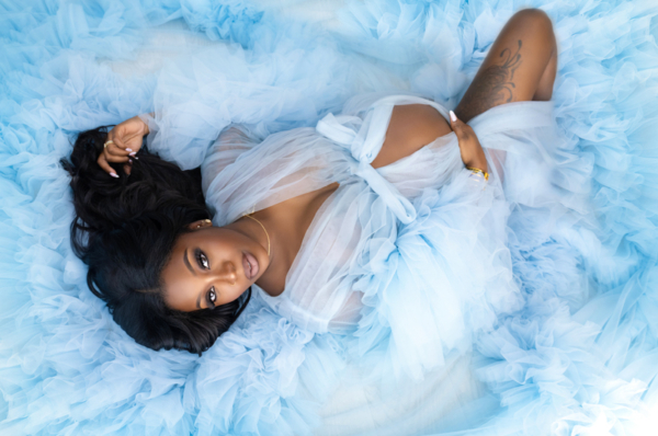Soft Elegance — Blue Couture Maternity Portrait Pregnant Black woman lying on a bed of soft blue tulle, wearing