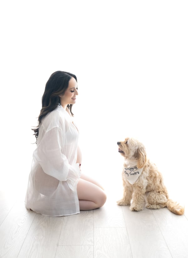 Mom-to-Be with Her First "Baby" Pregnant woman in white robe kneeling on the floor, smiling at her dog