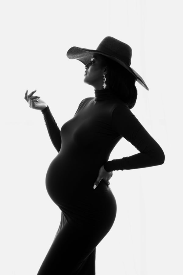 Minimalist Glamour — Maternity Silhouette in Hat Black-and-white silhouette of a pregnant woman wearing a wide-brimmed hat and celestial backdrop