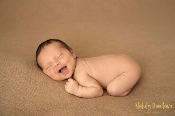 Smiling newborn baby lying on stomach on tan blanket &mdash; Washington DC newborn photography.