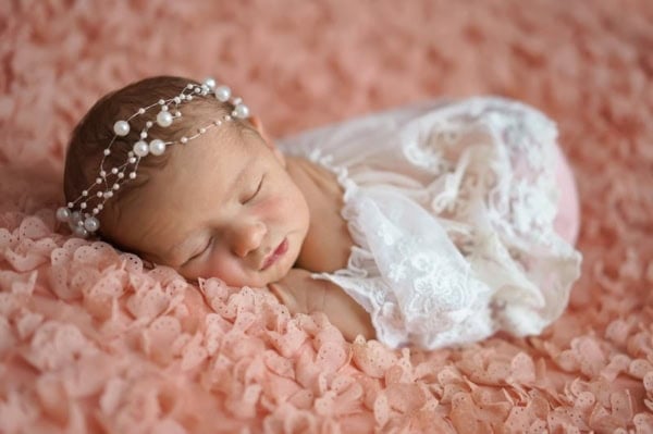 Newborn baby girl in lace dress and pearl headband sleeping on a peach blanket &mdash; Washington DC newborn photographer.