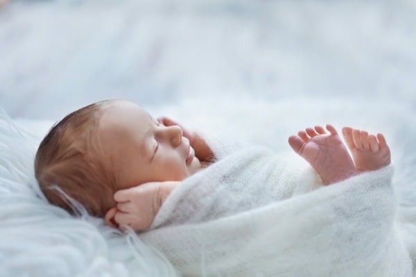 Side view of a sleeping newborn wrapped in a white blanket on a soft fur surface, photographed by Washington DC newborn photographer.