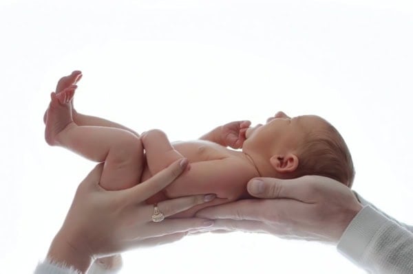 Newborn baby held in parents&rsquo; hands against bright white background &mdash; Washington DC newborn photography.