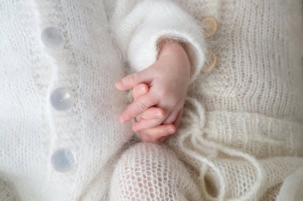 Close-up of newborn twins holding hands in white knitted outfits, photographed by Washington DC newborn photographer.