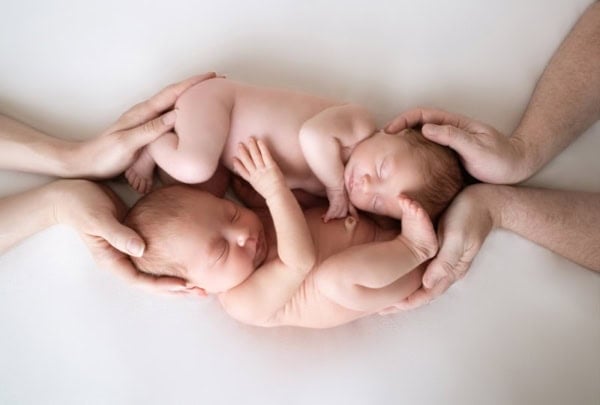Washington DC twin newborn photographer studio portrait of two naked sleeping newborn twins gently held by their parents&rsquo; hands, forming a ten