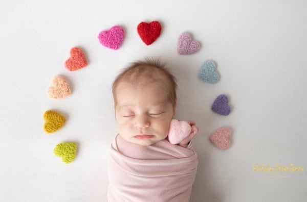 Newborn baby wrapped in pink blanket surrounded by colorful knitted hearts &mdash; Washington DC newborn photography.