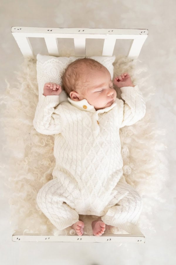 Newborn baby in a white knit outfit sleeping on a miniature bed with fluffy bedding &mdash; Washington DC newborn photographer.