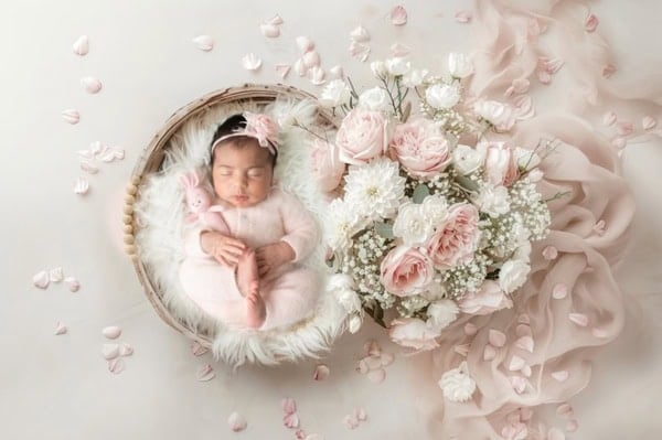 Newborn baby girl in pink knit outfit sleeping in basket with pastel flowers &mdash; Washington DC newborn photography.